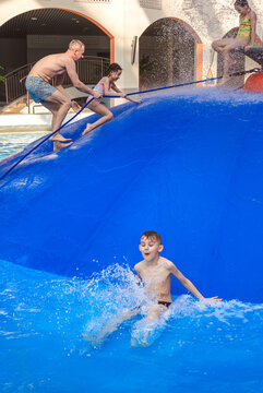 Group of happy people jumping from a blue water mushroom fountain dome at an indoor water park