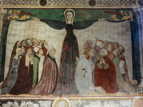 A historic medieval wall fresco depicting the Virgin Mary spreading her protective cloak over kneeling believers, clergy, and figures of nobility, framed by decorative borders.