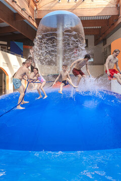 Large group of happy people jumping from a blue water mushroom fountain dome at an indoor water park