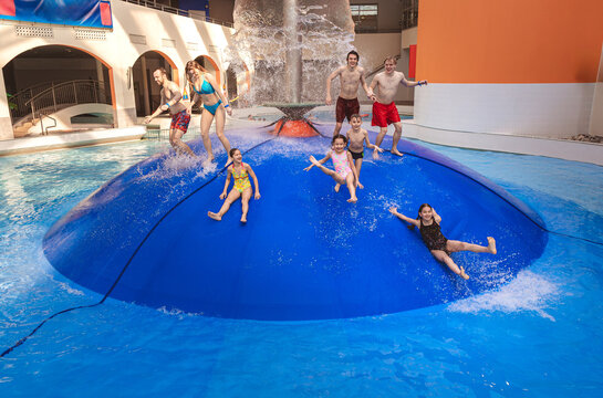 Large group of happy people jumping from a blue water mushroom fountain dome at an indoor water park