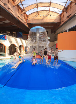 Large group of happy people jumping from a blue water mushroom fountain dome at an indoor water park