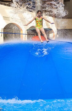 Group of children jumping from a blue water mushroom fountain dome at an indoor water park