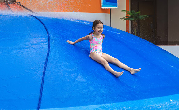 Group of children jumping from a blue water mushroom fountain dome at an indoor water park