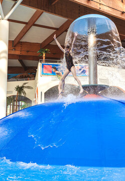 Group of children jumping from a blue water mushroom fountain dome at an indoor water park