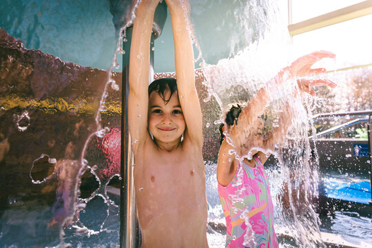 Happy young girl and boy hiding behind a water mushroom fountain spray at an indoor water park