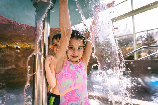 Happy young girl and boy hiding behind a water mushroom fountain spray at an indoor water park