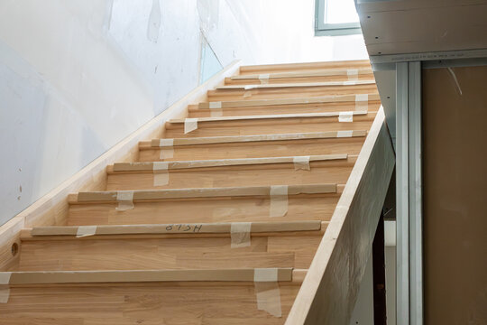 Escalier int&eacute;rieur en cours de r&eacute;novation avec marches en bois clair et bandes de protection adh&eacute;sives, illustrant un chantier propre et contemporain de r&eacute;novation domestique.