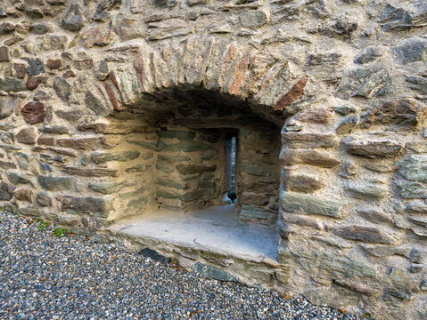 Close-up view of a historic fortress defensive masonry wall, featuring a small stone-arched embrasure with a narrow vertical arrow slit or loophole for defense.