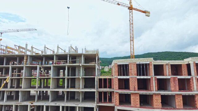 Multi story building under construction with exposed brick and concrete floors, tower crane lifting materials, scaffold lines across facade, empty window frames