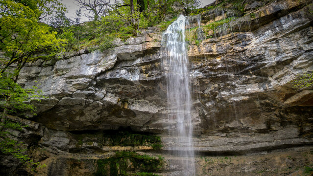 Aerial view of the Herisson waterfalls cascading down a rugged limestone cliff surrounded by lush green trees and mossy rocks in Menetrux-en-Joux, Bourgogne-Franche-Comte, France.