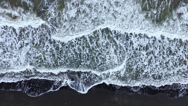 Water rolls in with waves that crash onto the sand, creating foam as the tide rises. The scene shows the natural movement of the sea near a beach.