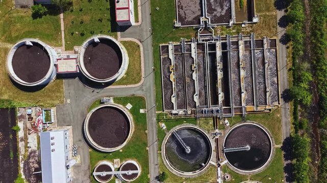 Aerial view wastewater treatment plant showing circular clarifiers, aeration tanks, sludge basins, rectangular settling lanes, maintenance buildings, service