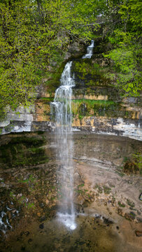 Aerial view of the Herisson waterfalls cascading over a steep limestone cliff surrounded by lush green forest in Menetrux-en-Joux, Bourgogne-Franche-Comte, France.