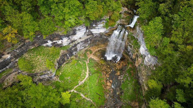 Aerial view of The Herisson waterfalls cascading down rocky cliffs surrounded by lush green forest and hiking trails in Menetrux-en-Joux, Bourgogne-Franche-Comte, France.