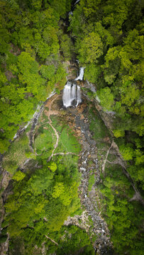 Aerial view of the Herisson waterfalls cascading through a lush green forest with rocky terrain and hiking paths in Menetrux-en-Joux, Bourgogne-Franche-Comte, France.