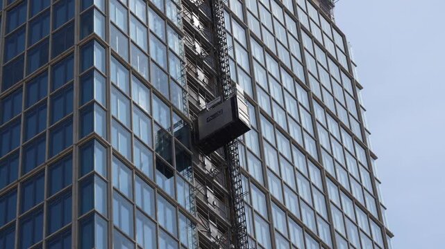 A construction lift climbs the facade of a modern glass office building in Berlin. Reflective windows, scaffolding and geometric lines emphasize urban development.