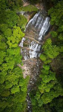 Aerial view of the Herisson waterfalls cascading over rocky cliffs surrounded by dense green forest in Menetrux-en-Joux, Bourgogne-Franche-Comte, France.