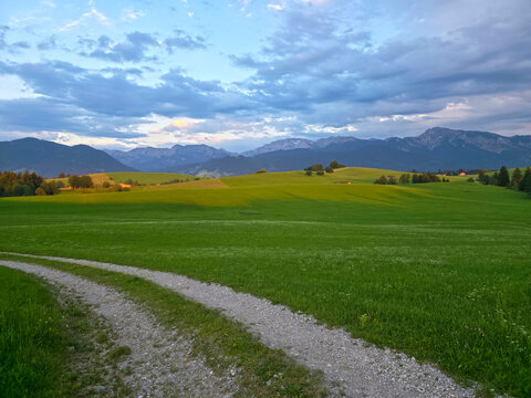 germany, sunlit hiking path crossing endless meadows toward distant alpine peaks and rolling hills