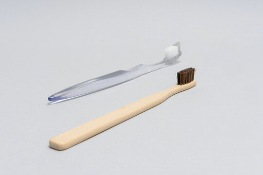 Bamboo toothbrush in foreground with plastic toothbrush blurred in background on gray surface