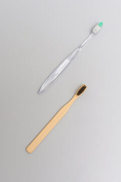Top view bamboo and plastic toothbrushes arranged diagonally on gray background eco comparison
