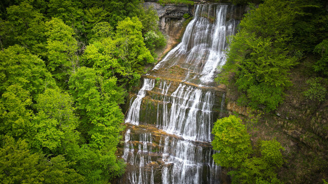 Aerial view of the multi-tiered Herisson waterfalls cascading down rocky cliffs surrounded by lush green forest in Menetrux-en-Joux, Bourgogne-Franche-Comte, France.