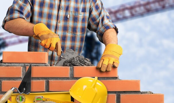Construction worker building a brick wall at a construction site with tools and gloves