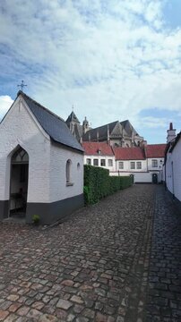 Historic UNESCO Courtrai beguinage forward walk revealing white heritage houses and the towering Gothic church in soft daylight.