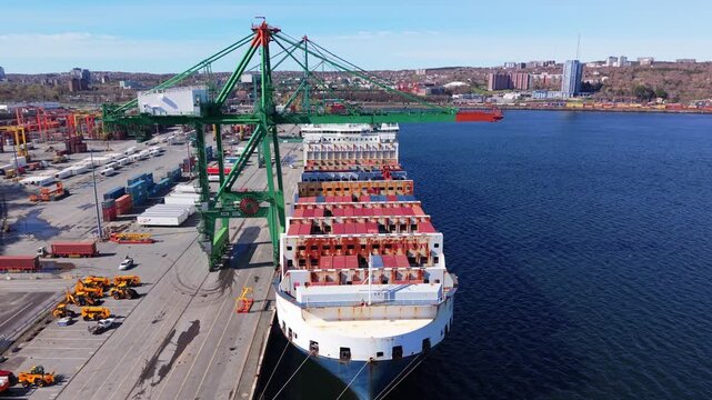 Witness the dynamic operations at Nova Scotia's container port where cargo ships await loading and unloading under bright skies, showcasing the beauty of maritime trade