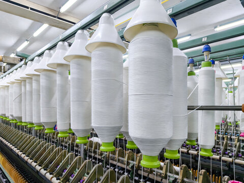 Rows of large white yarn spools with green bases on textile machine