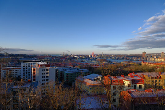 wide-angle high-angle view of Gothenburg cityscape from Masthugget hill illuminated by sunlight, red roof buildings, distant harbor river, and a blue sky.