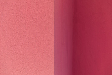 Fototapeta premium A textured wall surface painted in contrasting shades of dark and light pink divided by a vertical line, abstract background, minimalist design, vibrant color contrast.