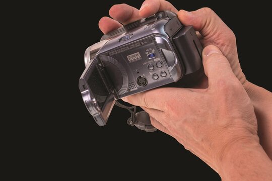 Close up view of hands holding JVC digital video camera isolated on black background. Sweden. 