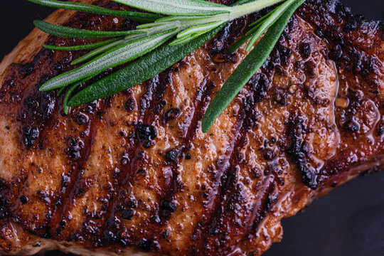 Close up a of grilled steak is placed on a dark plate. Fresh green herbs sit a top the meat. top view
