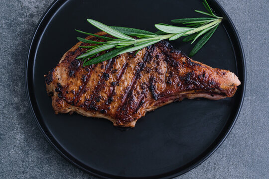 Grilled meat served on a black plate with fresh herbs on top on a concrete background. The juicy meat features distinct grill marks and a golden-brown crust. top view