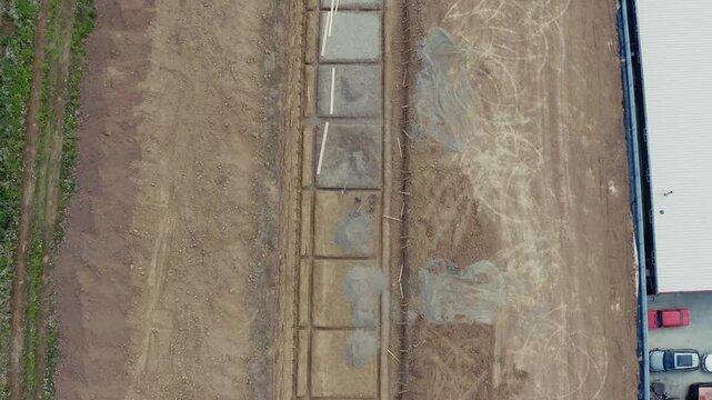 Straight-down aerial drone shot of concrete strip foundation footings laid in excavated trench at active residential construction site with truck visible at edge. Perfect for construction and real est