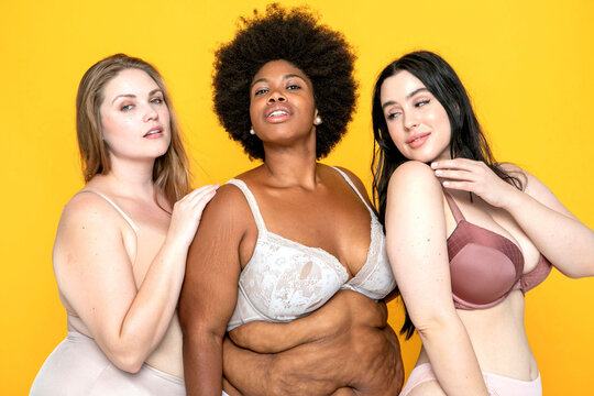 Three women in lingerie pose confidently against a yellow background.