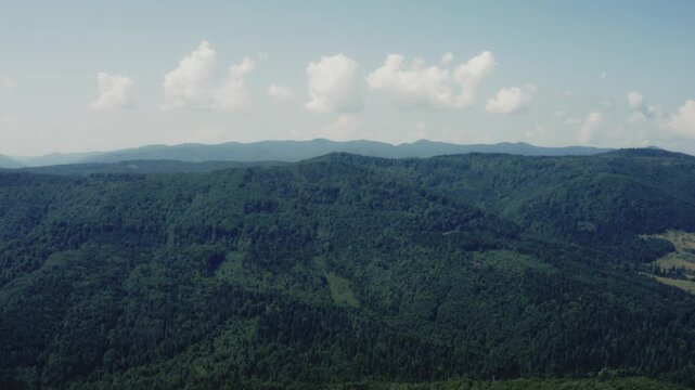 Wide cinematic aerial drone shot of vast Carpathian mountain range with layered forested ridges stretching to the horizon under blue sky with white clouds. Perfect for nature, travel, Ukraine, and lan