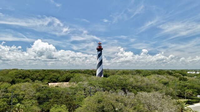 Aerial view of the St. Augustine Lighthouse with its iconic black and white spiral stripes rising above lush green trees on Anastasia Island, St. Johns County, Florida, United States.