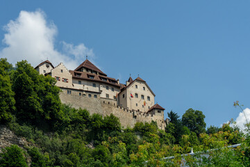 Fototapeta premium Exterior of Vaduz castle in Liechtenstein on top of the mountain seen from below during summer - the sky is blue with white clouds, the sun is shining