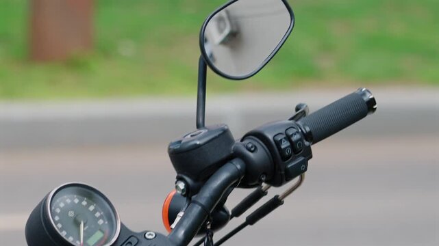 Close up shot of motorcycle handlebar with mirror and controls on blurry background.