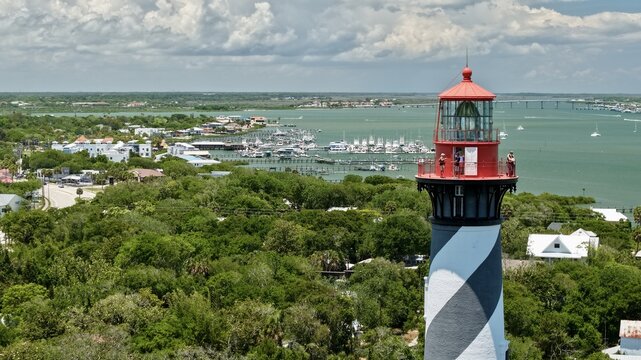 Aerial view of the St. Augustine Lighthouse with black and white spiral stripes and people on the observation deck overlooking the harbor in St. Johns County, Florida, United States.