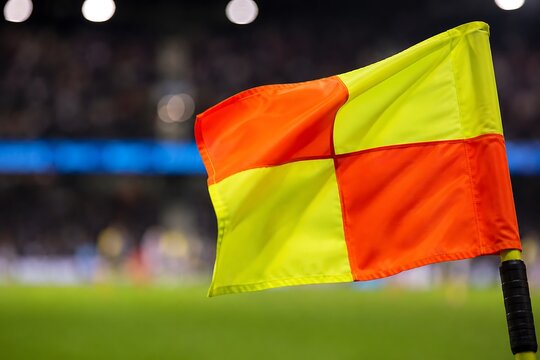Macro sports shot of a yellow and orange offside flag waving during a tense football match, shallow depth of field.