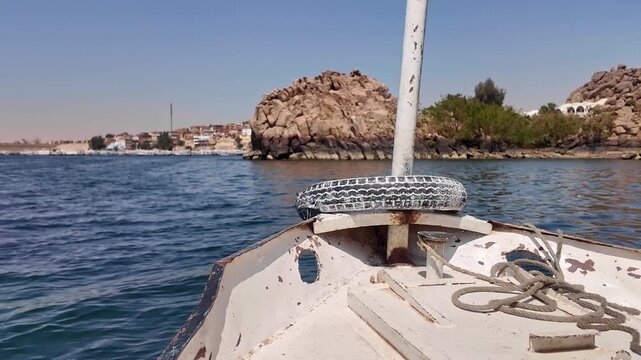 Point of view from a traditional boat sailing on the calm blue water of the nile river towards the historic philae temple in aswan, egypt