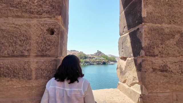 Tourist woman looking at the beautiful landscape of the nile river from a window in the ancient philae temple, a landmark in aswan, egypt