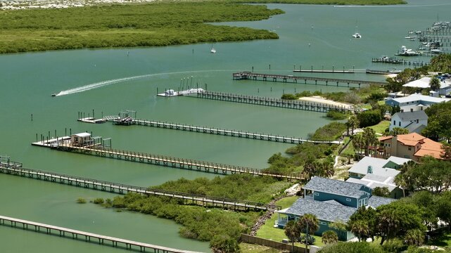 Aerial view of Anastasia Island featuring long wooden piers extending into the calm waterway past waterfront houses and lush green mangroves in St. Johns County, Florida, United States.
