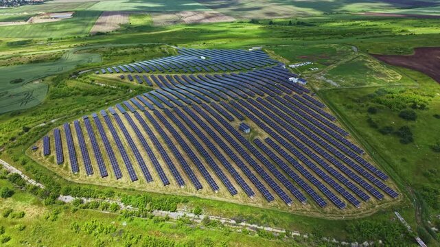 Aerial view solar panels in field, triangular utilityscale array on green meadow, morning light highlighting rows of photovoltaic modules, gravel access path