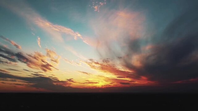 The golden and orange rays of the setting sun burn the edges of the clouds, contrasting with the fading blue sky and the thick, slowly moving gray clouds.