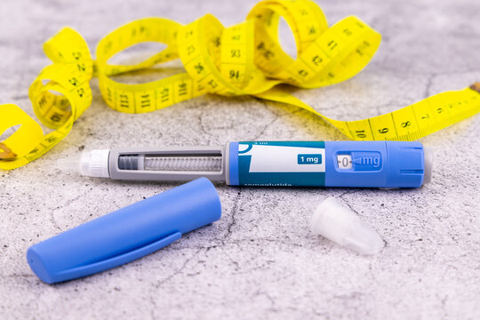 Medical semaglutide glp1 injection pen beside disposable needles and a yellow tape measure displayed on a grey marble background