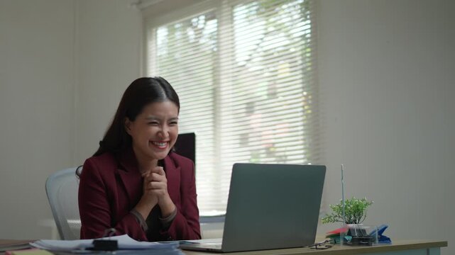 Successful young professional woman feeling ecstatic and raising her arms in victory while looking at her computer screen in the office