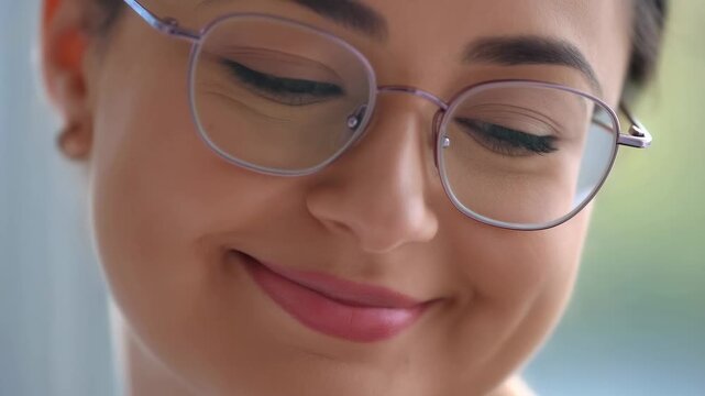 Close-up of a young woman smiling gently while wearing glasses. Capturing a moment of joy and contentment in everyday life